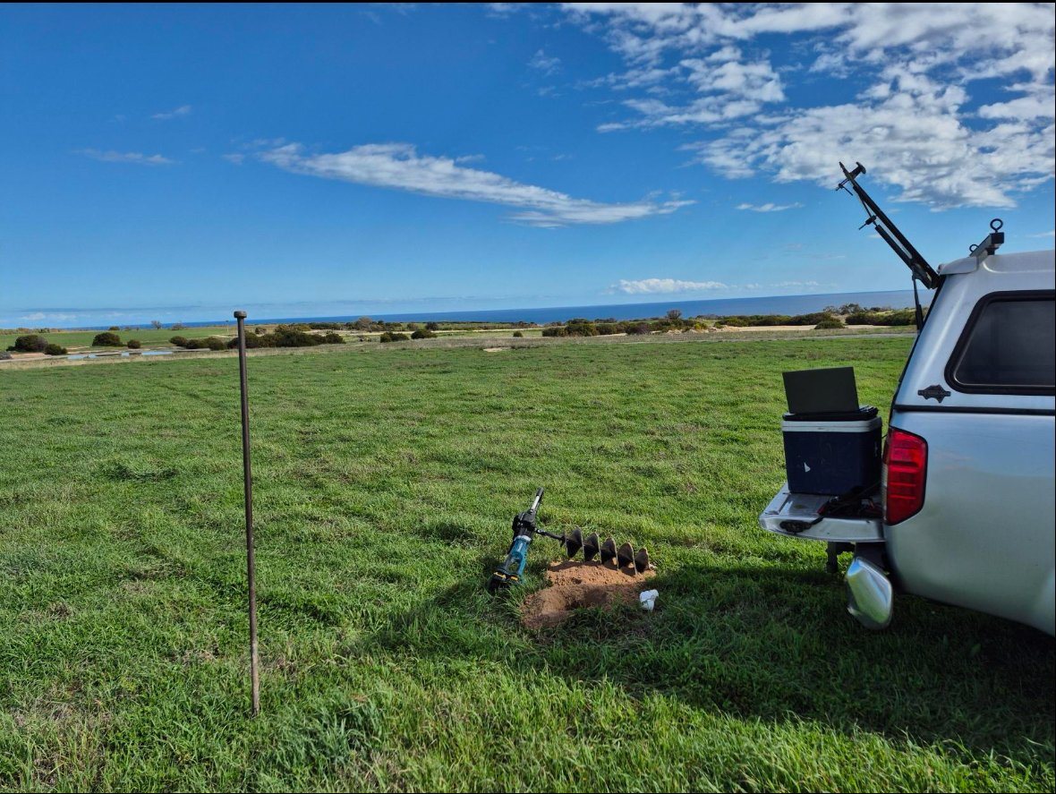 Field sampling setup — power auger boring on coastal grassland with Gulf St Vincent visible in the background