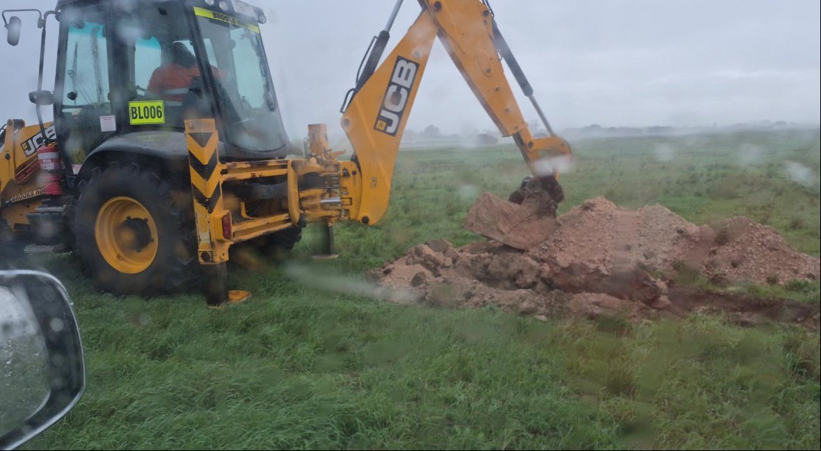 JCB backhoe excavating test pit in wet conditions
